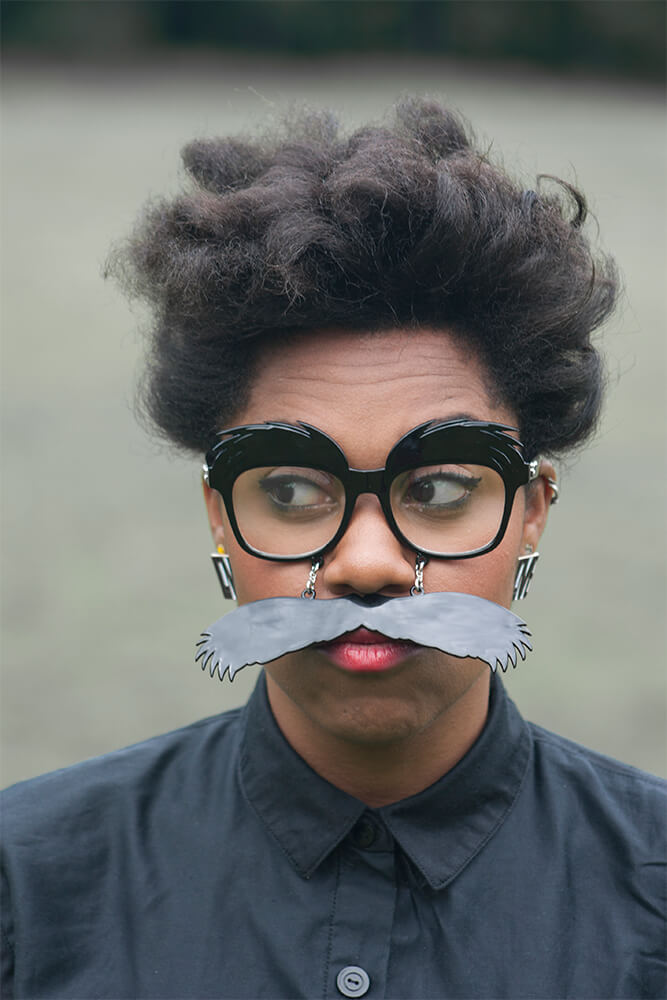 Keisha is wearing comical glasses and a moustache. Her expression is quizzical. Image Credit - Ray Fiasco