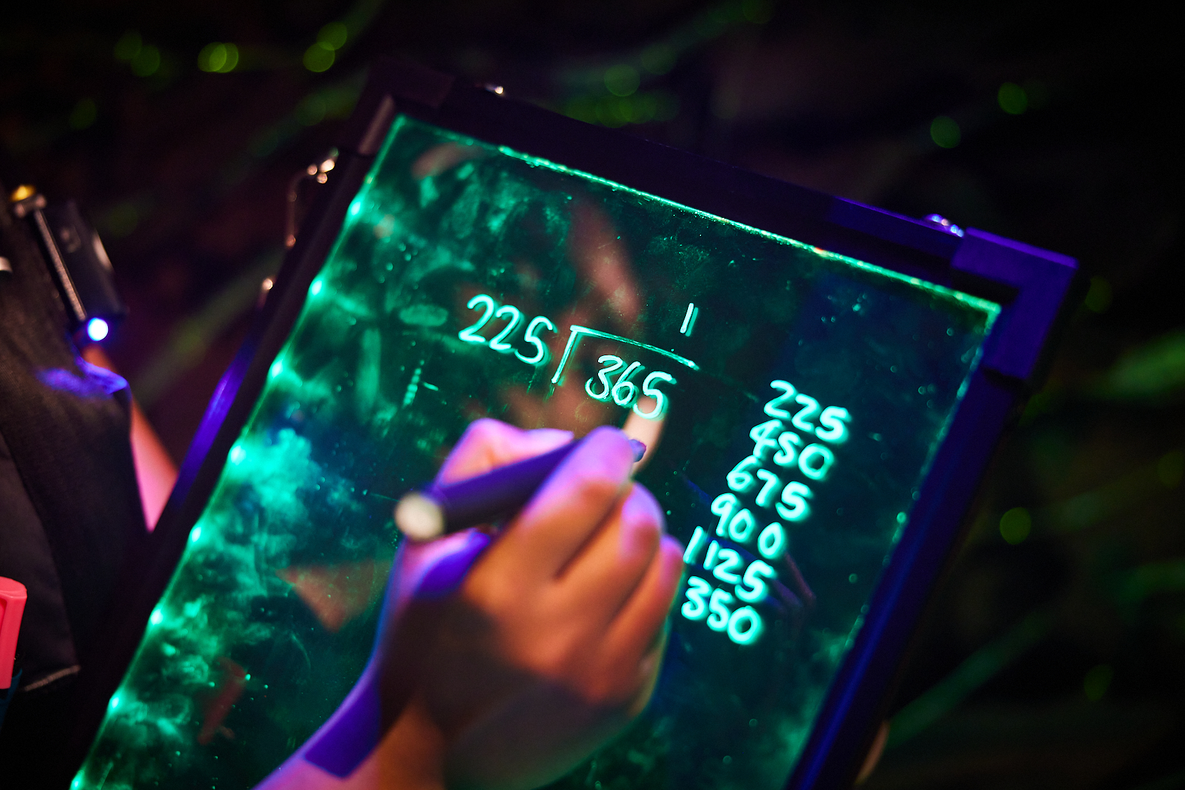 Maths problem being solved on a glass neon board